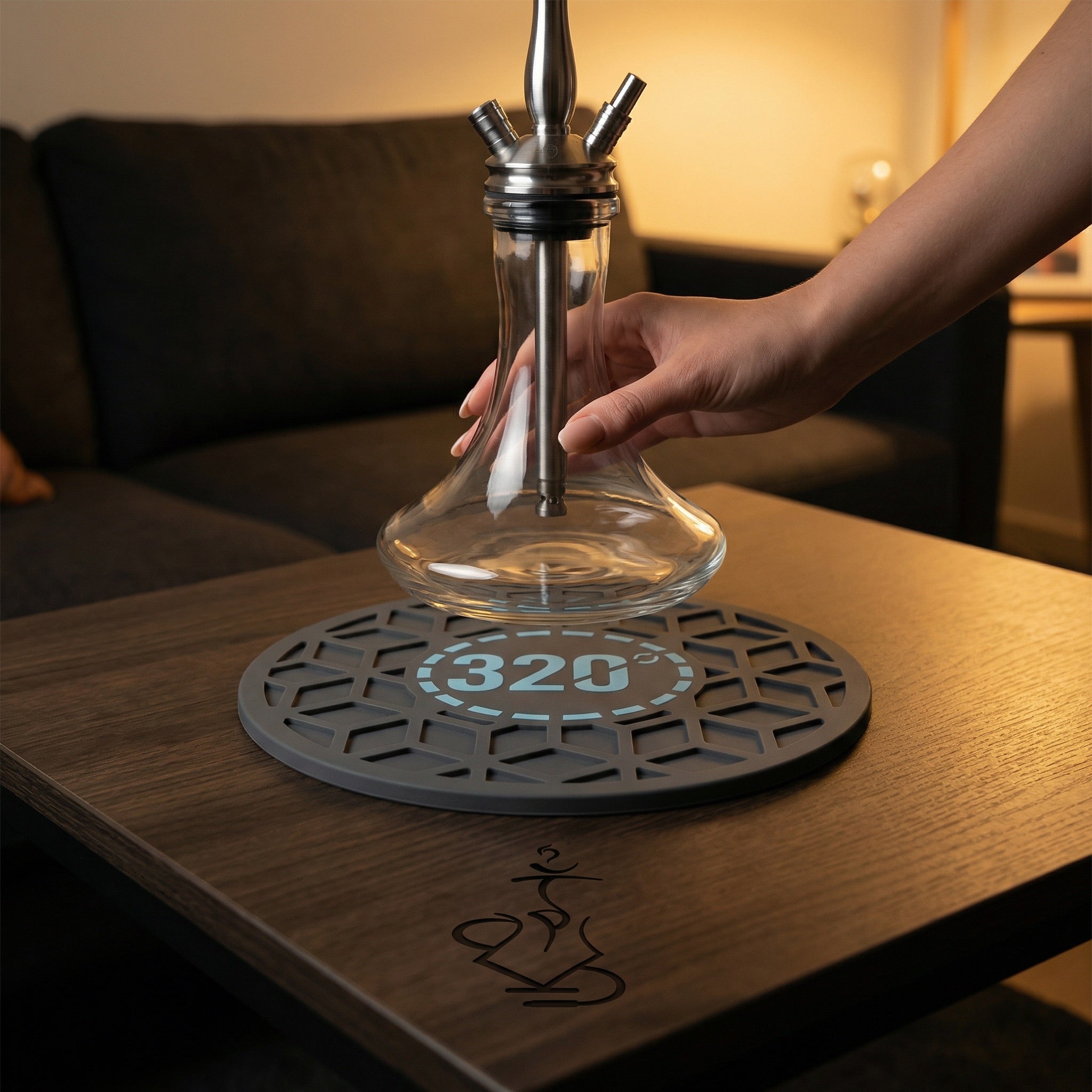 320° Hookah Base Mat Black & Blue placed on a dark timber lounge table with a glass hookah base being set down onto the grip surface, showing the mat in a real session setup.