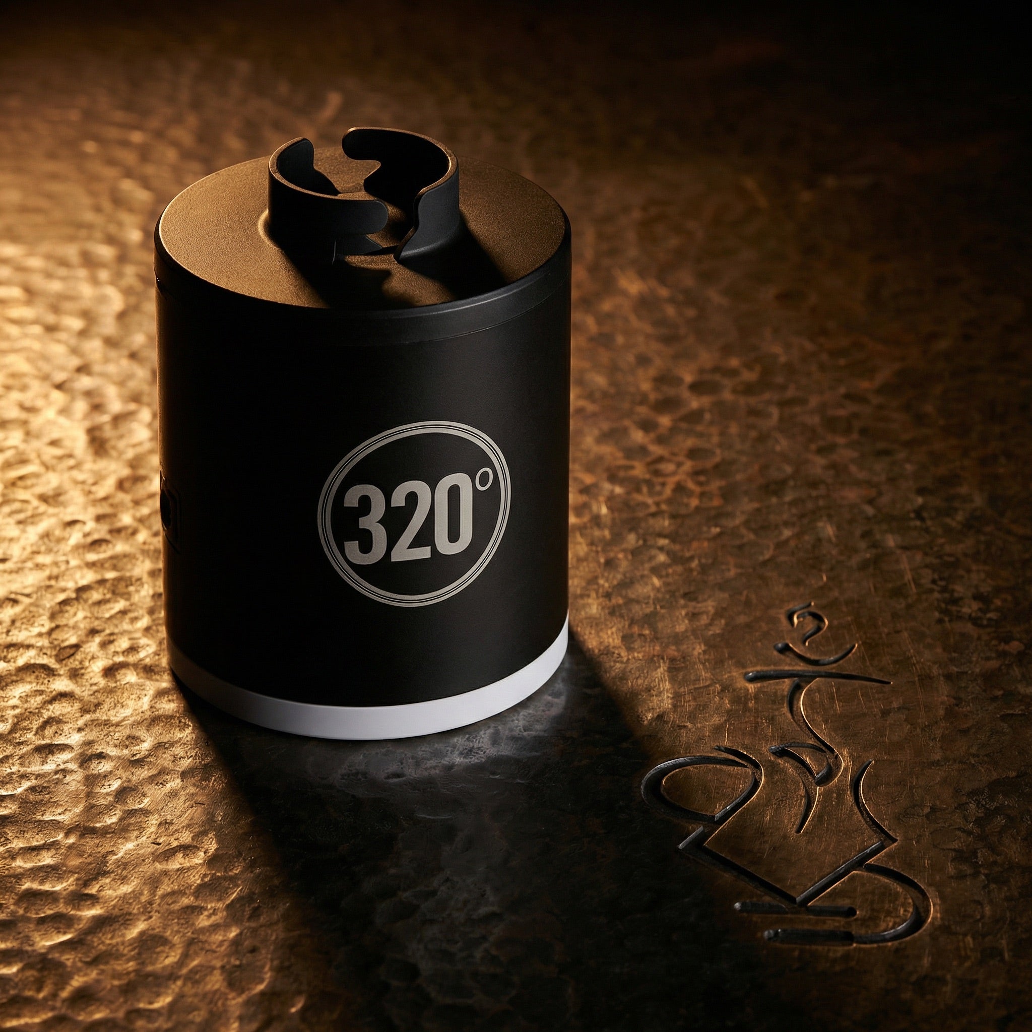 320° LED electric shisha starter pump lit dramatically on a warm hammered bronze surface, showcasing the matte black cylindrical body and circular 320° badge in a dark editorial hero shot.