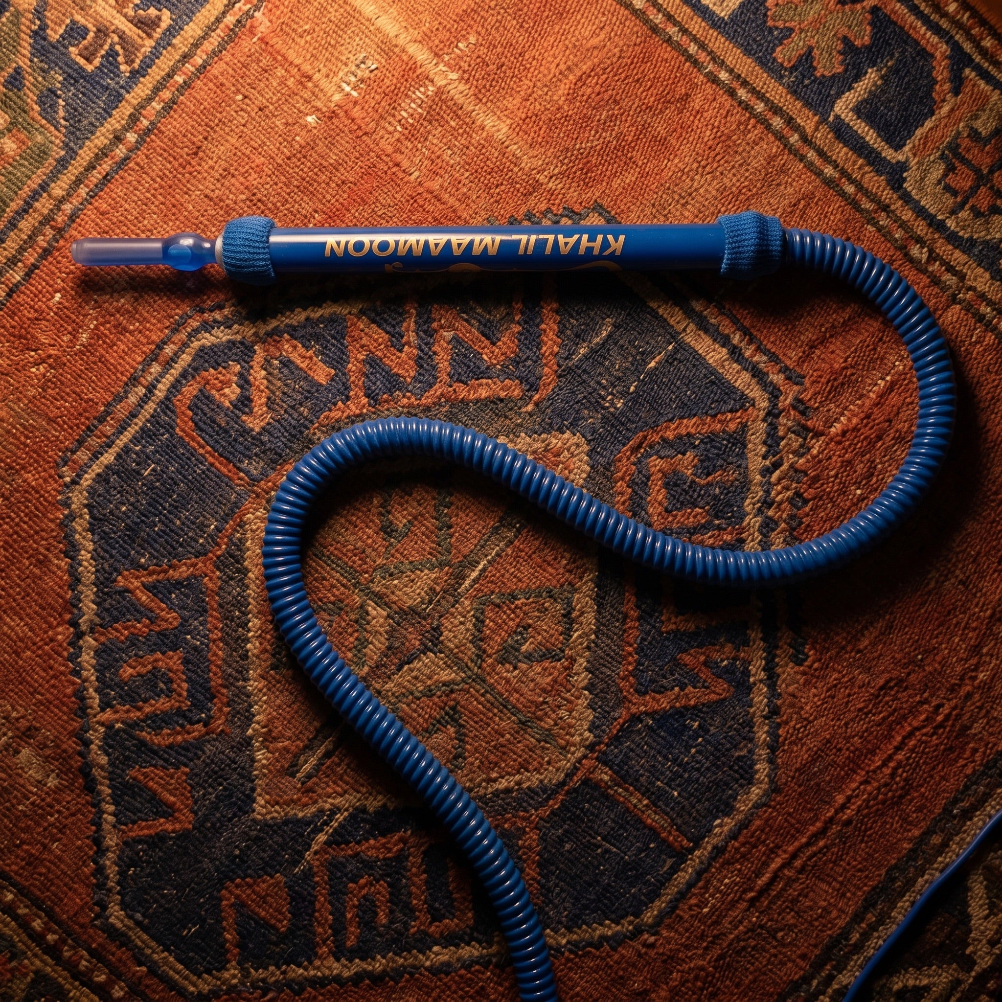Khalil Mamoon Blue Shisha Hose resting on a warm Persian kilim in a quiet majlis setting