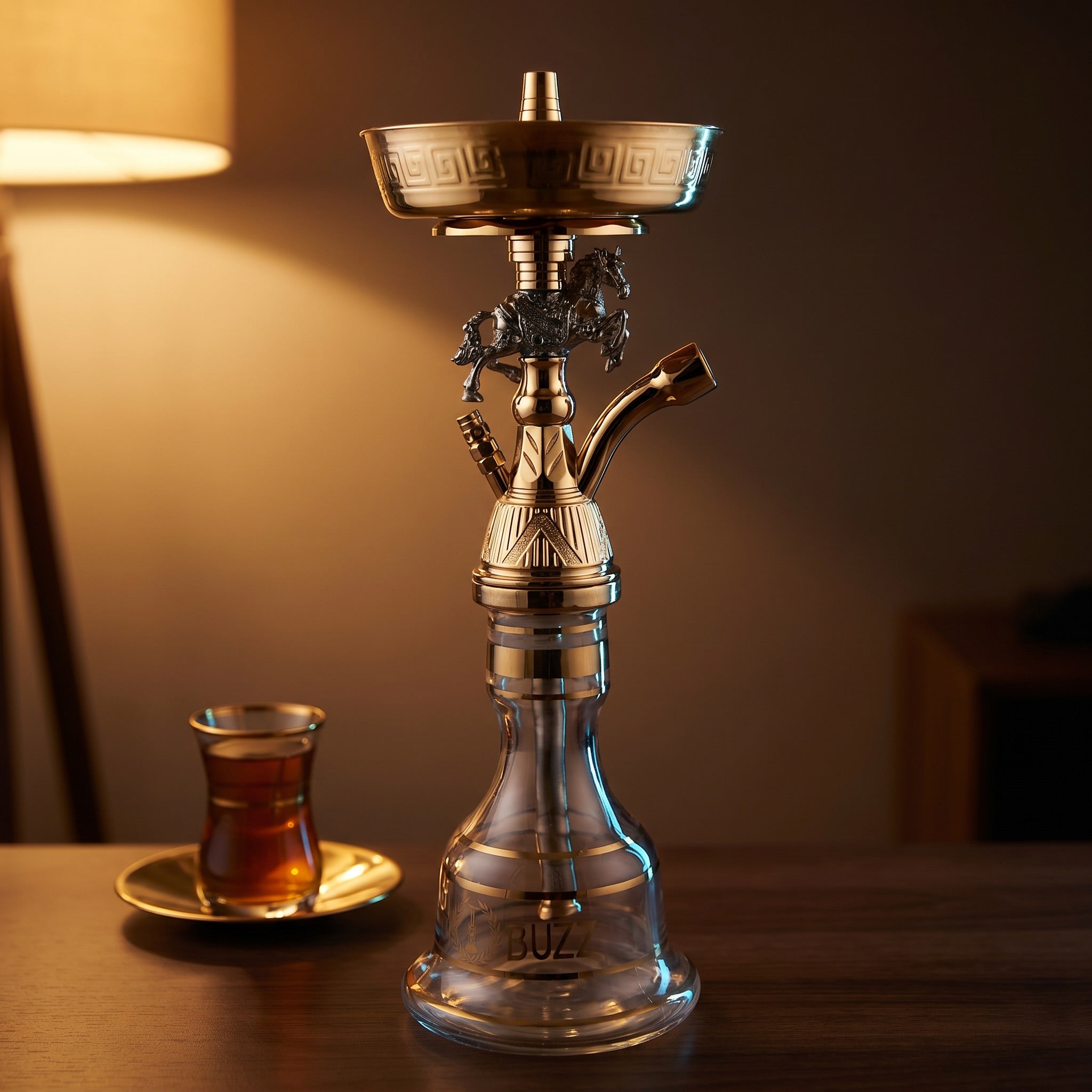 Basha Buzz Mustang shisha pipe on walnut surface beside a glass of amber tea in a warm home lounge