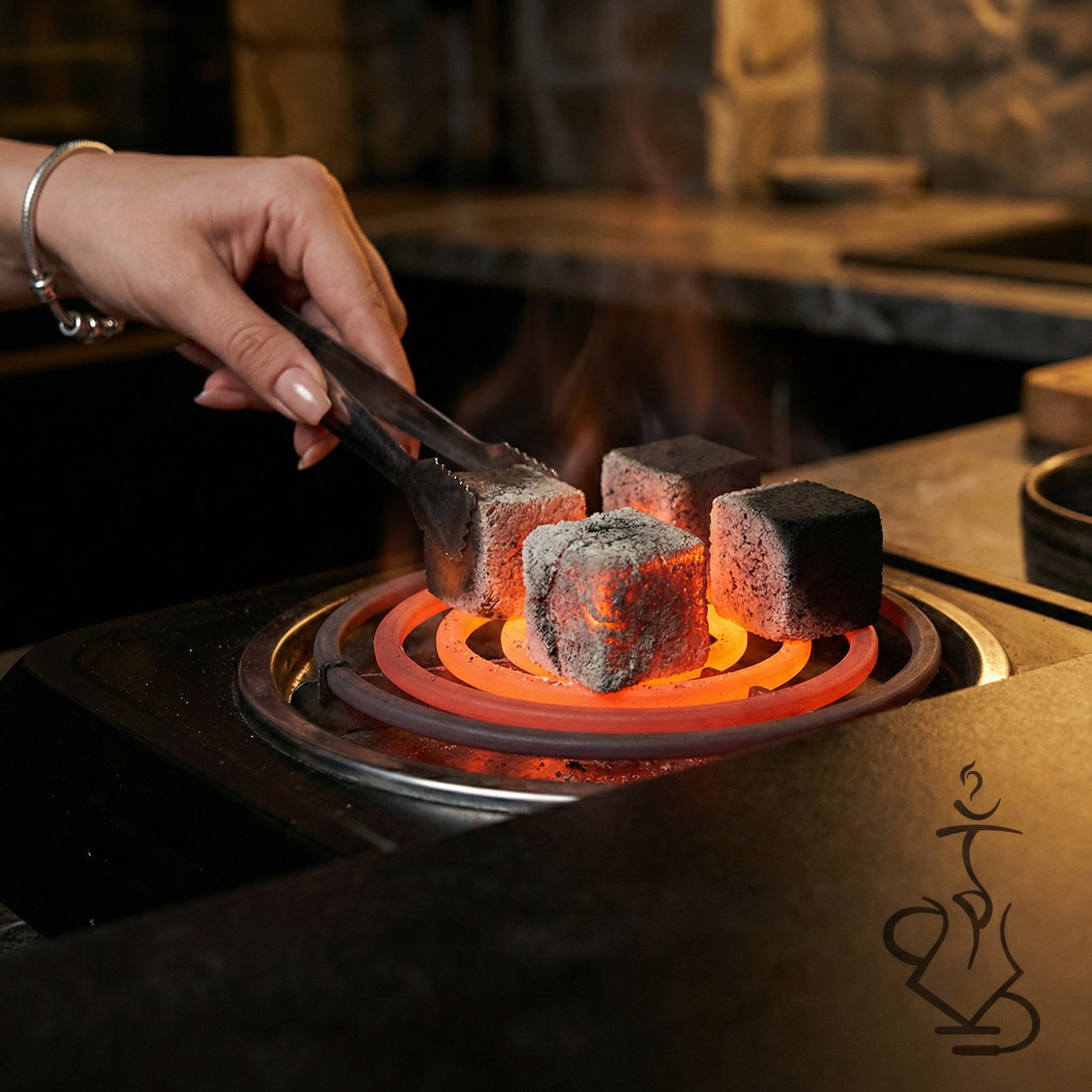 Cerberus Coco 26mm coconut shisha charcoal cubes at various stages of ignition on a glowing electric burner coil, hand with tongs flipping a partially lit cube.
