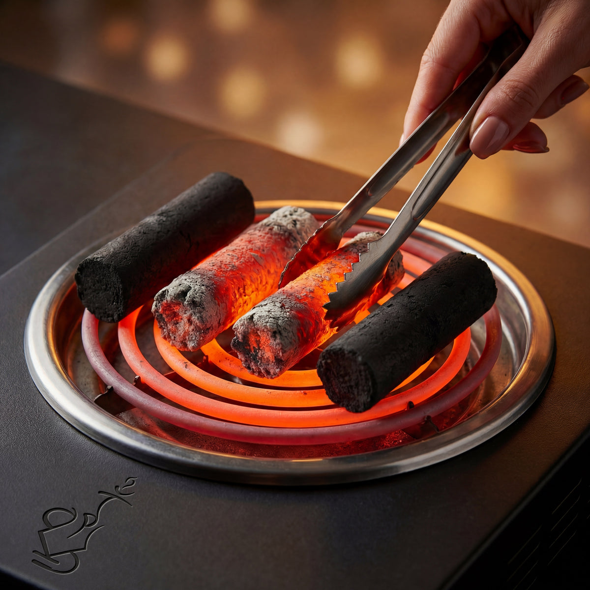 Cocosupreme Fingers coconut charcoal pieces lighting on an electric burner coil with a hand rotating a piece using tongs in a warm ambient session prep setting., image 3 of 12