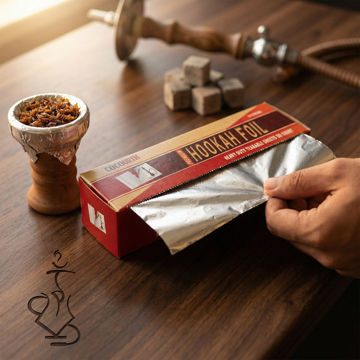 Cocourth Heavy-Duty Shisha Foil being dispensed from the box during hookah bowl preparation, showing clean tear from built-in cutter on a walnut countertop, image 2 of 5