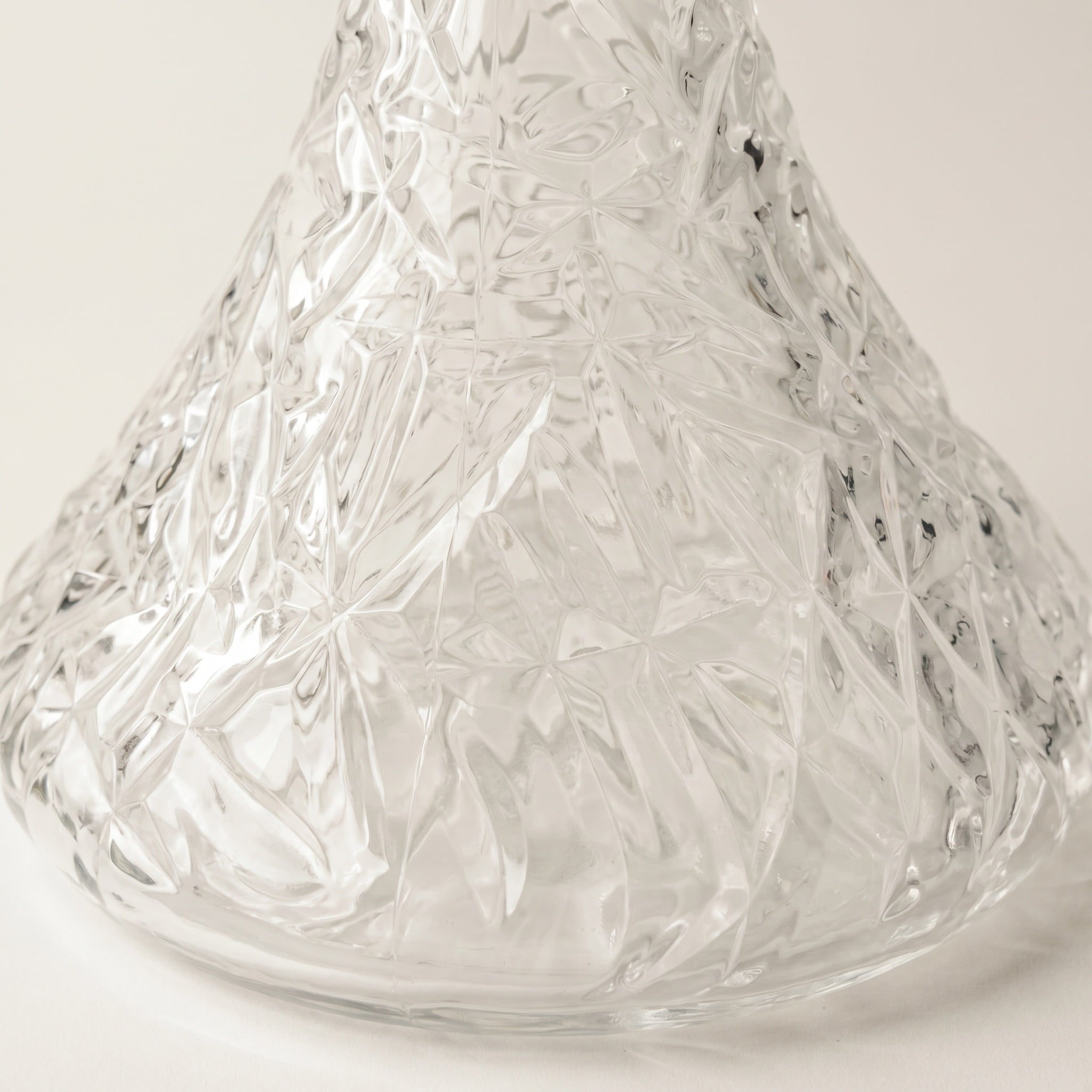 Essentials Crystal-Cut Clear Russian shisha vase on travertine plinth, refracted light fanning across the wall behind
