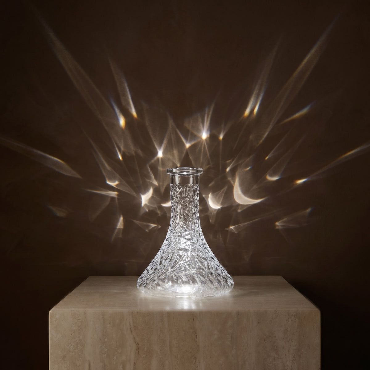 Essentials Crystal-Cut Clear Russian shisha vase on travertine plinth, refracted light fanning across the wall behind, image 3 of 4