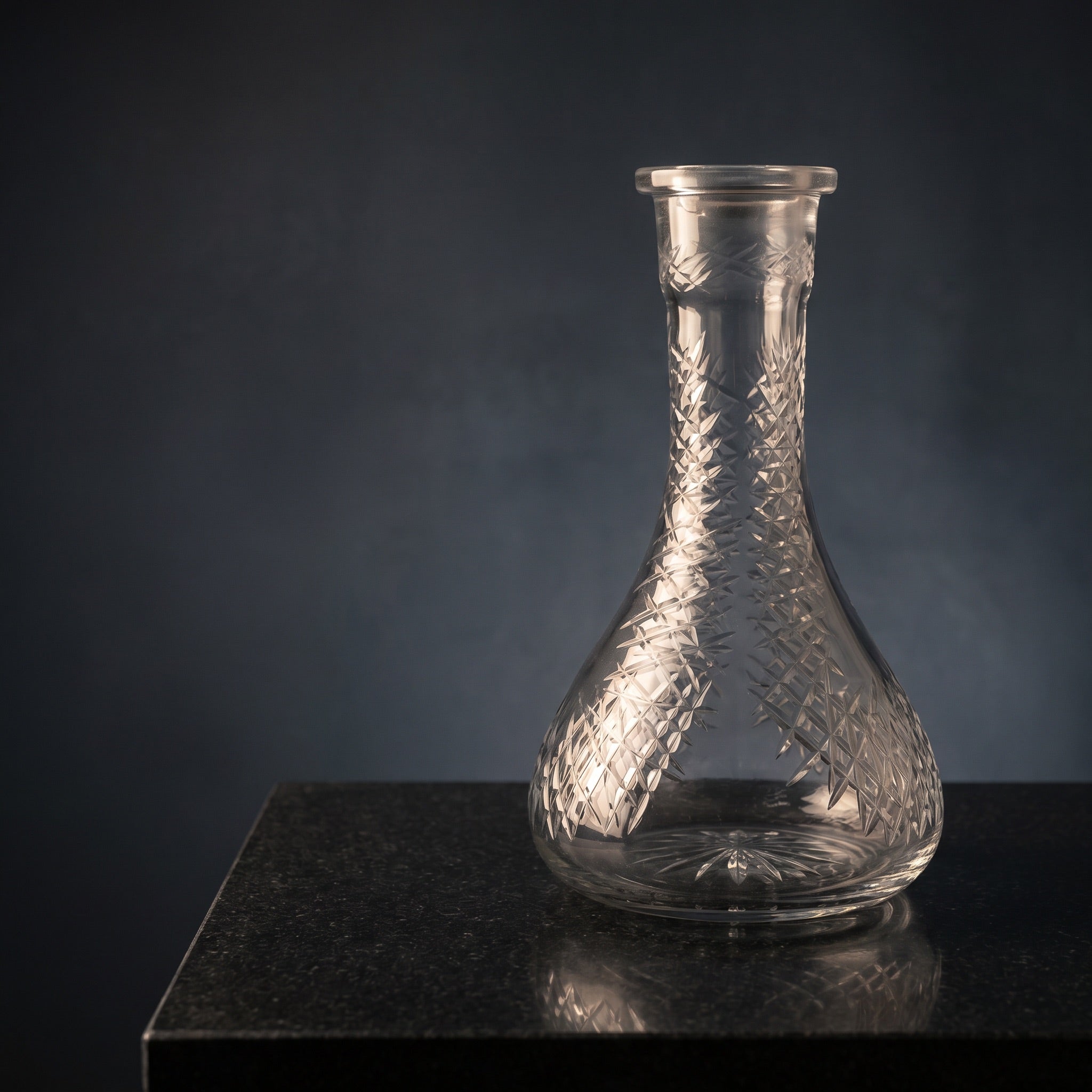 Essentials Etched Diamond Clear shisha vase on polished dark stone, warm key light catching the diamond hatch cuts across the clear glass body