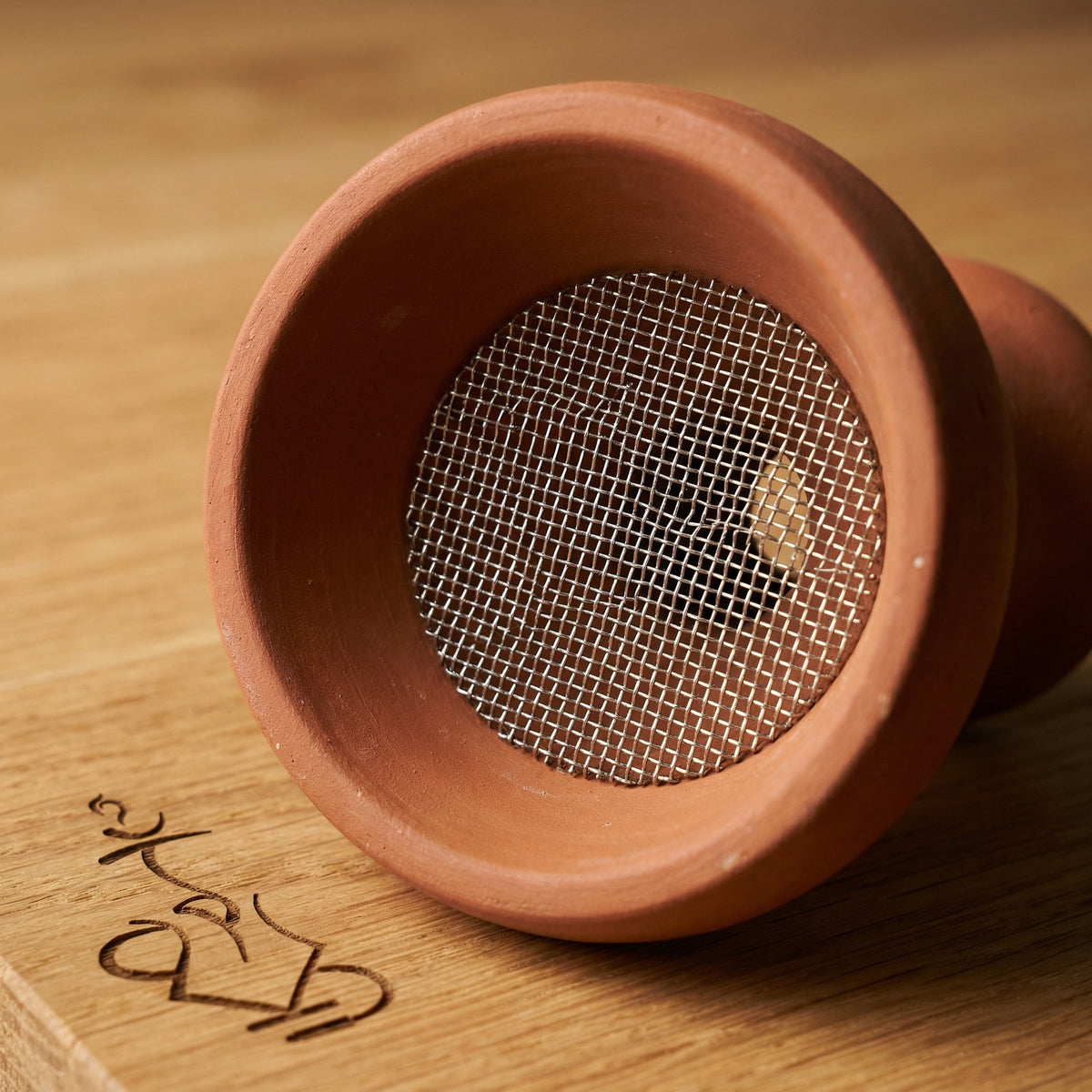 Essentials stainless mesh insert seated flat inside a traditional multi-hole Egyptian clay shisha bowl, showing the fit and coverage over the draw holes for cleaner base water., image 4 of 6
