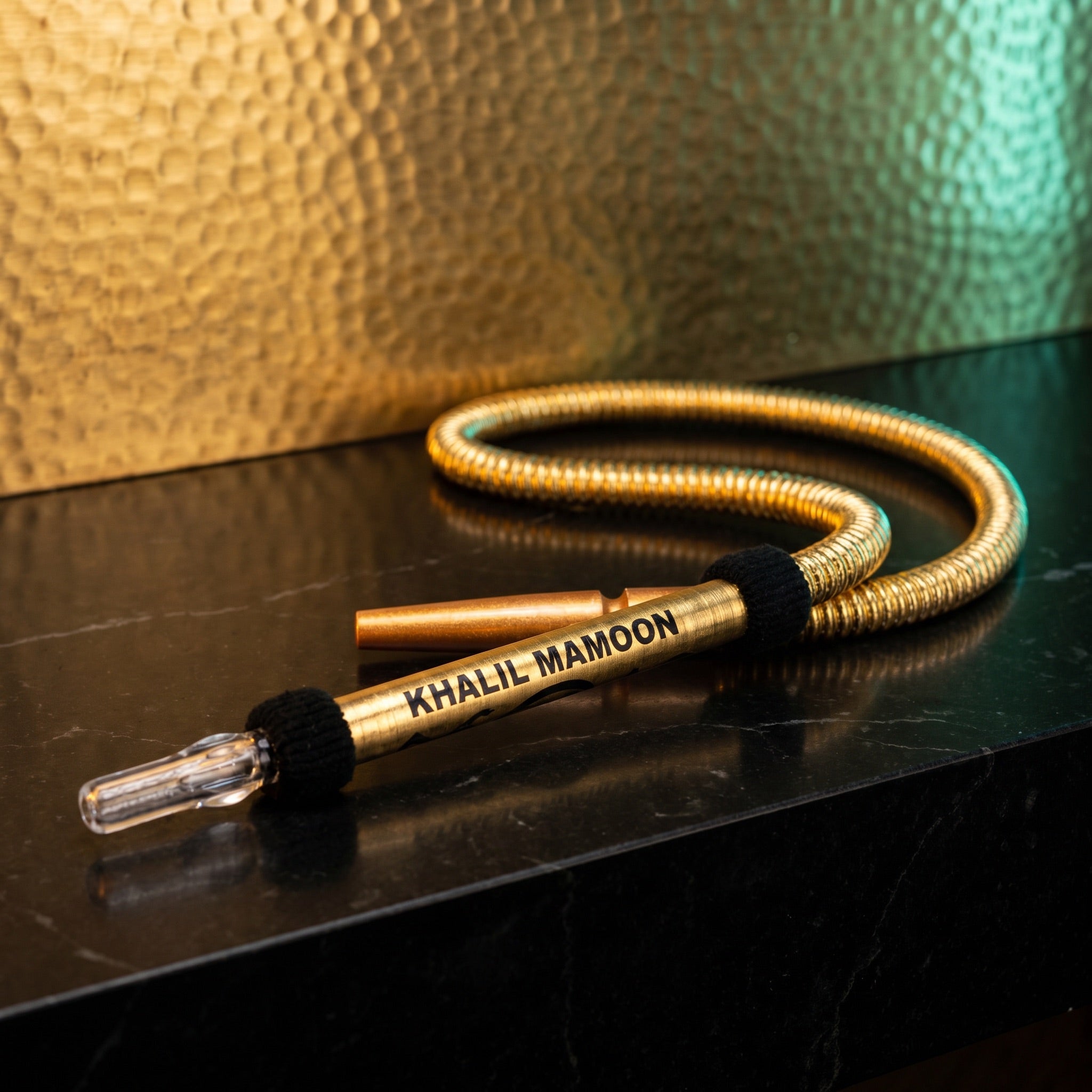Khalil Mamoon Gold Washable Hose on polished black stone with hammered gold backdrop and teal rim light