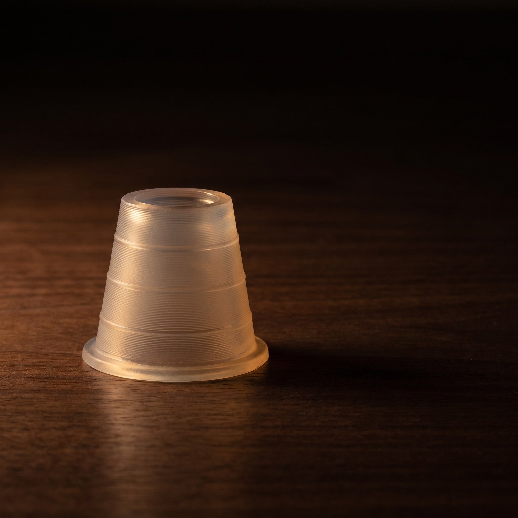 Khalil Mamoon hose grommet glowing softly under warm tungsten light on dark walnut surface, translucent rubber seal