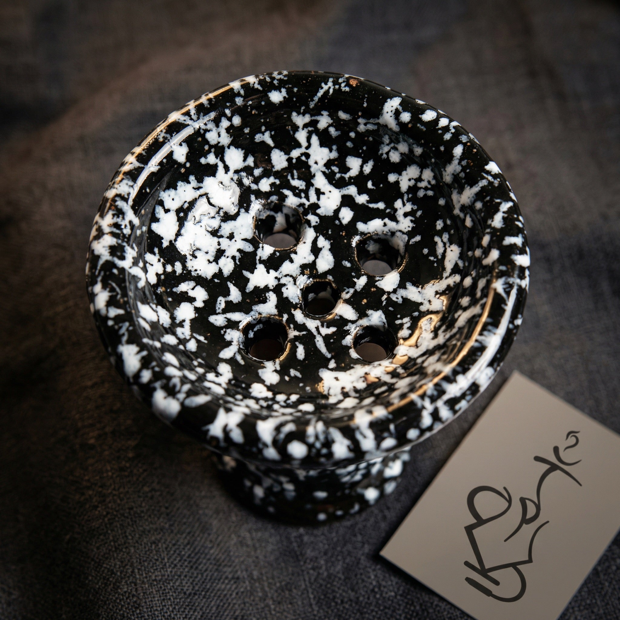 Top-down macro view of Khalil Mamoon marble ceramic bowl showing five-hole floor pattern and glossy black and white spatter glaze detail