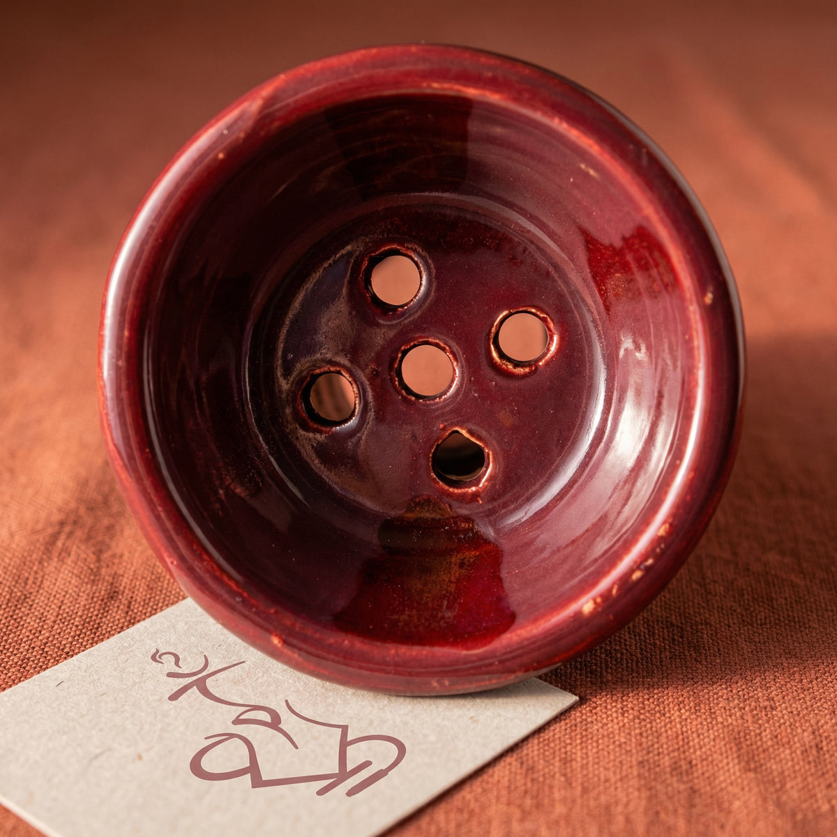 Top-down macro of the King Buzz Traditional Egyptian Bowl interior showing the 5-hole floor pattern and hand-dipped burgundy ceramic glaze texture., image 3 of 7