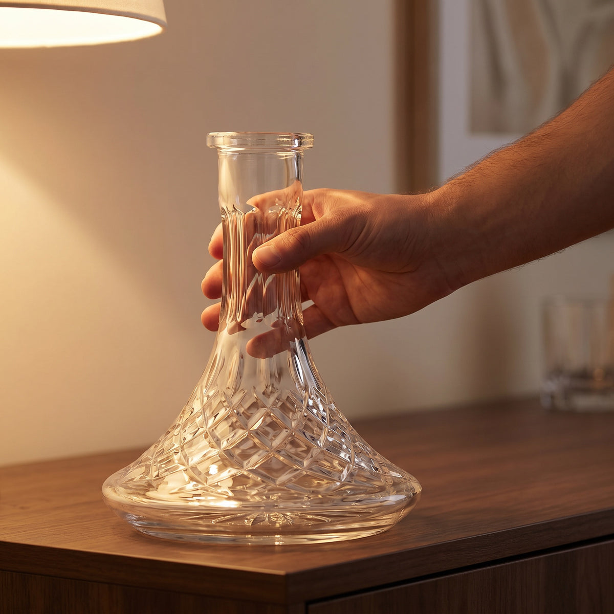 Hand lifting Lismore crystal-cut hookah base from dark wood sideboard in warm lamplit home setting, image 5 of 6