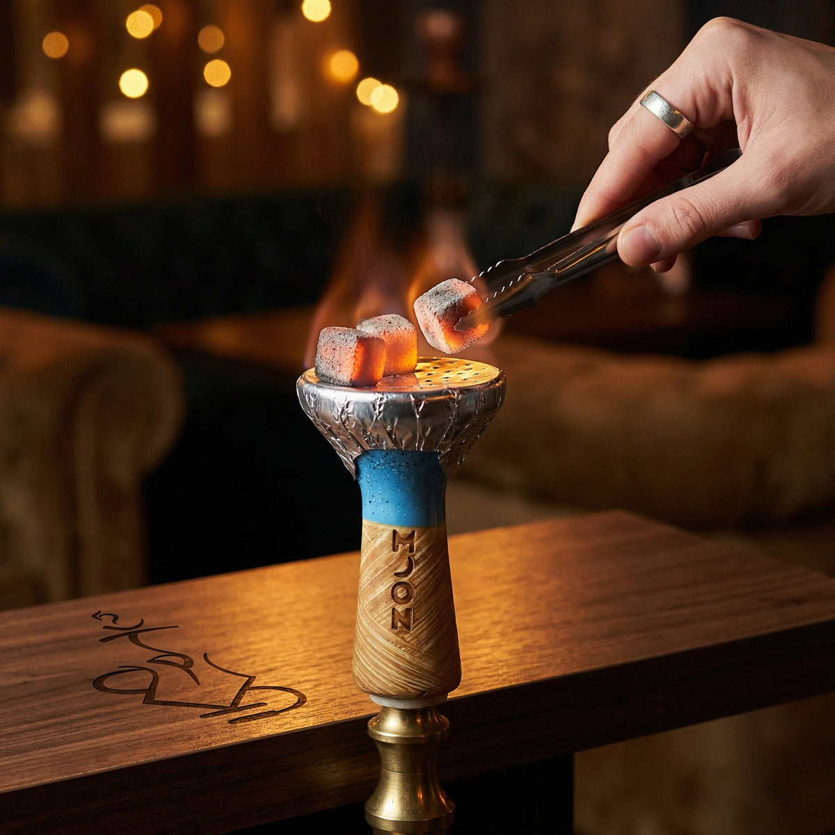 Moon Phunnel blue glazed bowl mounted on a hookah with foil and glowing coconut coals, set on a walnut table in a warm lounge environment with whisky and tongs alongside., image 3 of 11