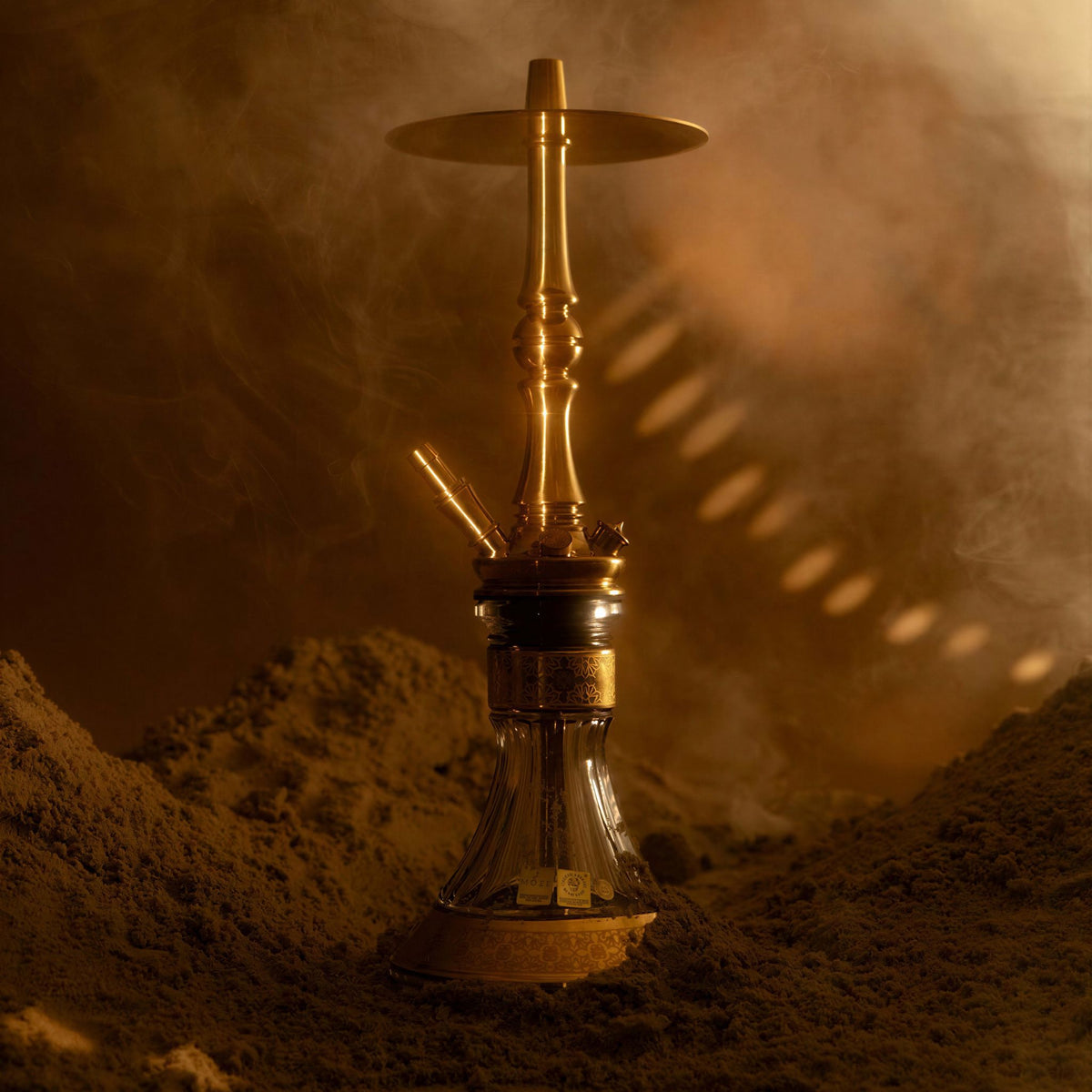 Moze Tradi M Gold traditional shisha in a warm smoky desert setting, polished gold stem on a cut-glass base, image 6 of 7