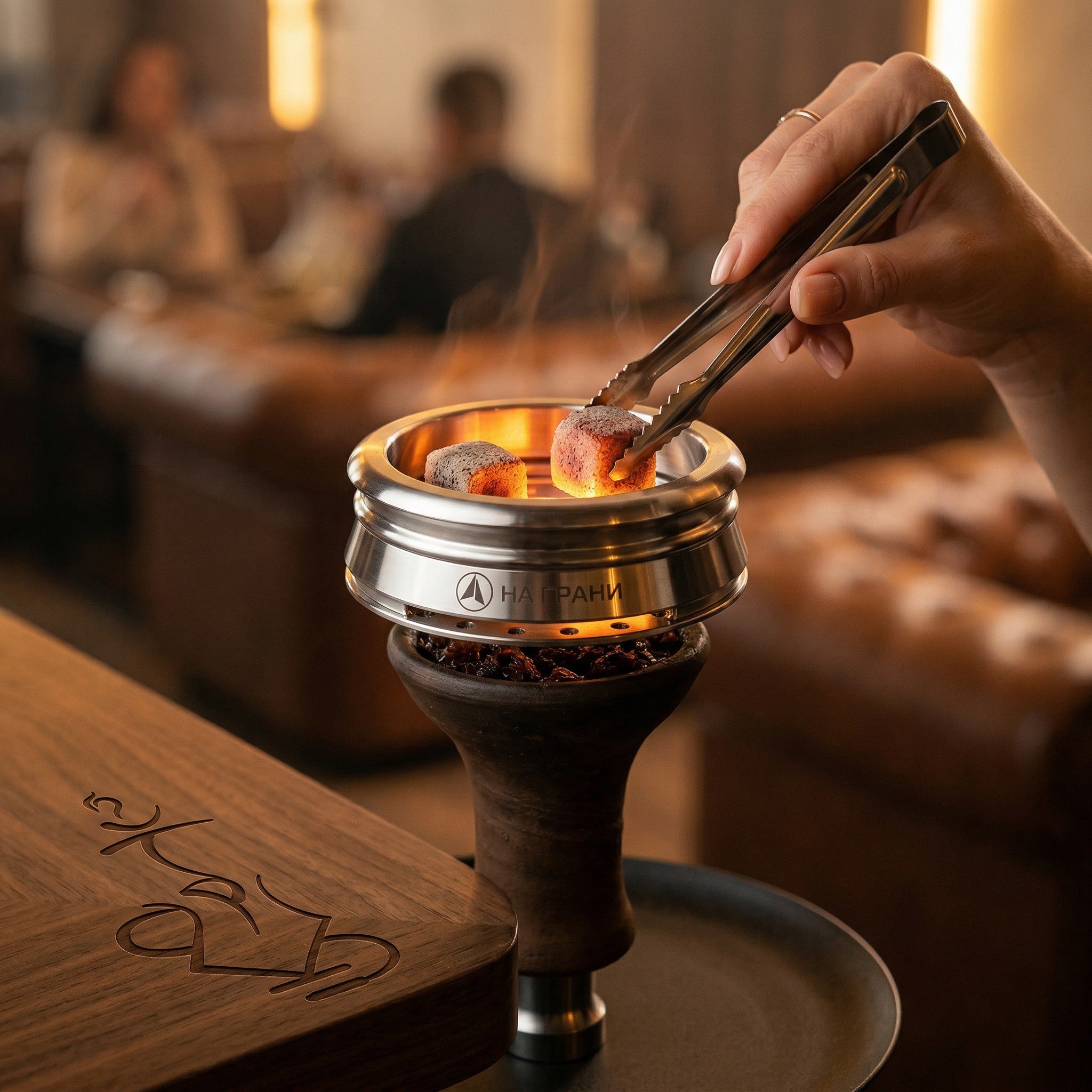 Na Grani On The Edge stainless steel HMD sitting on a hookah bowl with glowing coconut coals inside, warm lounge session setting