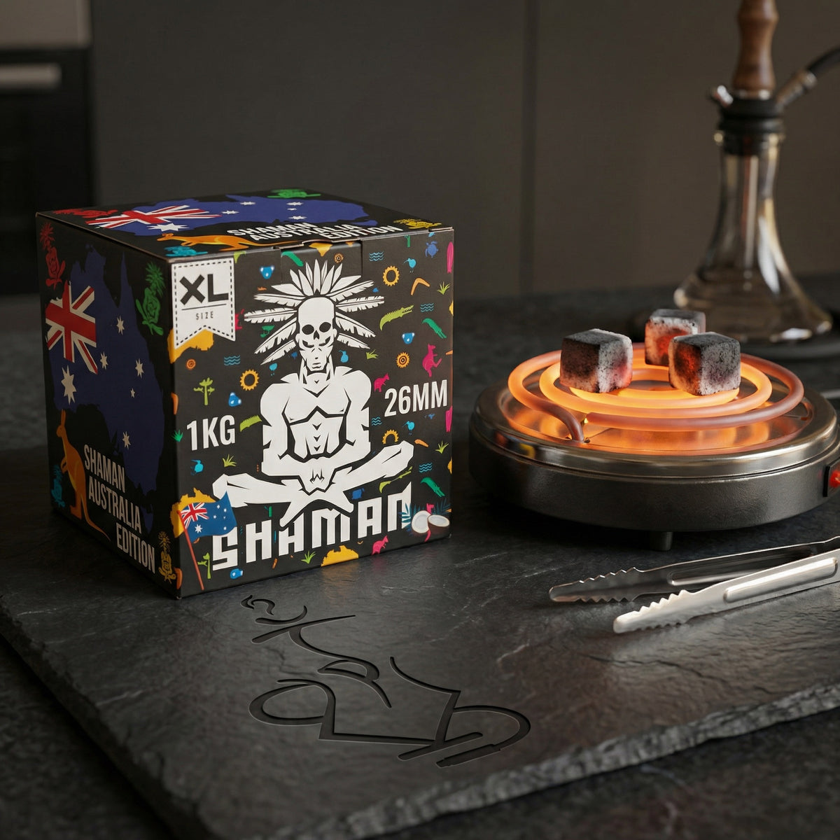 Shaman 26mm coconut charcoal 1kg box on a dark slate countertop beside an electric burner with glowing coals, tongs, and a hookah in the background., image 3 of 15