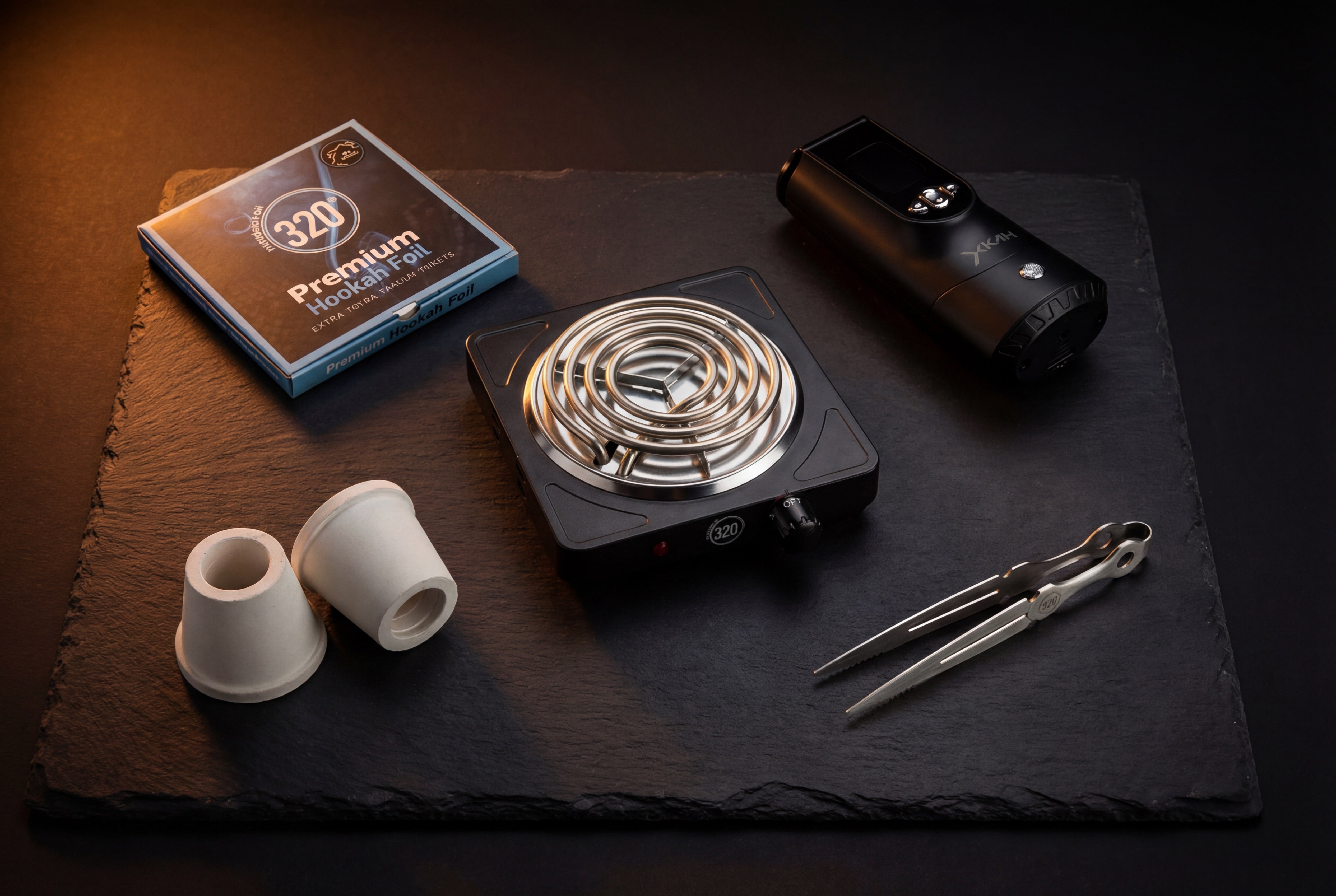 Shisha accessories flat lay including 320° charcoal burner, premium foil, XKAH Silver, silicone adapters and tongs on dark slate surface