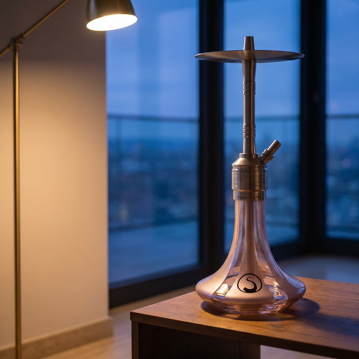 Steamulation Mini Gen II Rose Metallic on walnut table in modern apartment at dusk, brass lamp light, city view, image 3 of 10